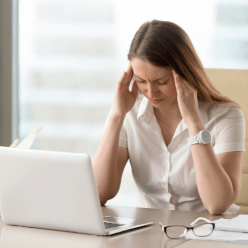 Woman sitting at a desk holding her temples indicating a tension-type headache.