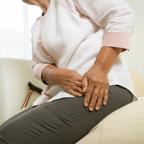 Older woman holding the front of the hip and groin area indicating pain from psoas tendinopathy.