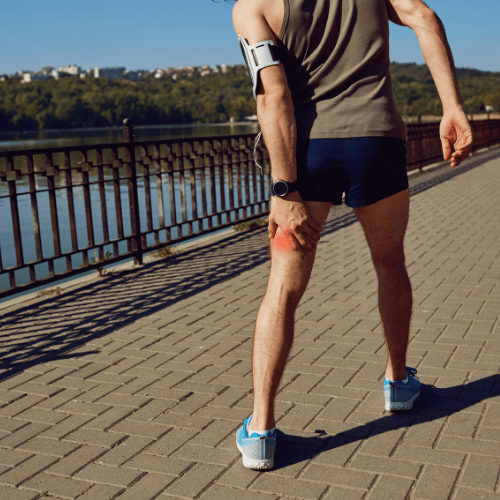 Runner holding the back of the thigh with highlighted pain indicating a hamstring strain.