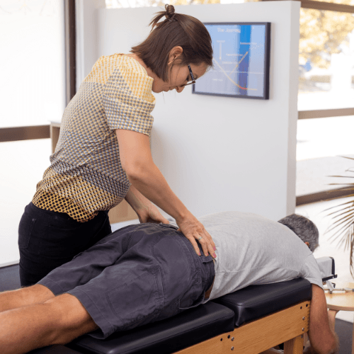 Chiropractor performing a sacroiliac joint adjustment on a patient lying face down on a treatment table.