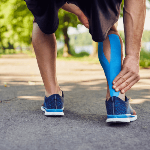 Runner holding the back of the ankle with kinesiology tape applied over the Achilles tendon to illustrate Achilles tendinitis symptoms.