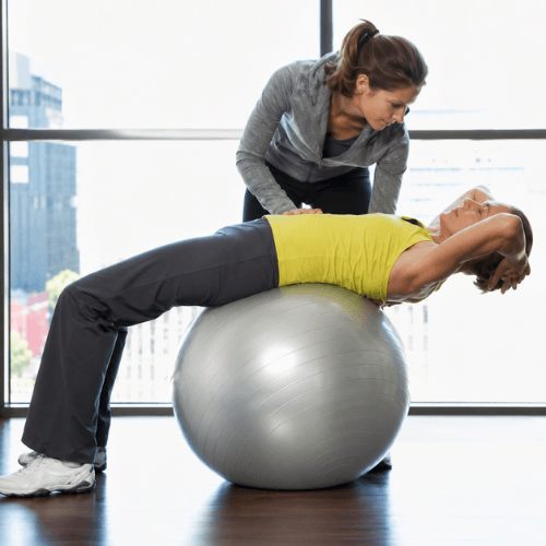 Physical therapist guiding a patient through therapeutic exercise on a stability ball for sciatica rehabilitation.