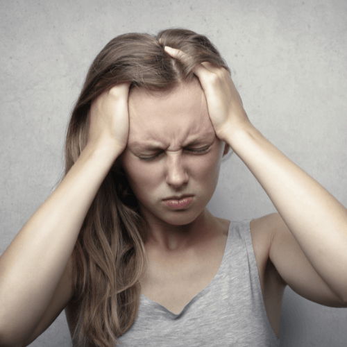 Woman holding both sides of her head while experiencing intense headache pain and discomfort.