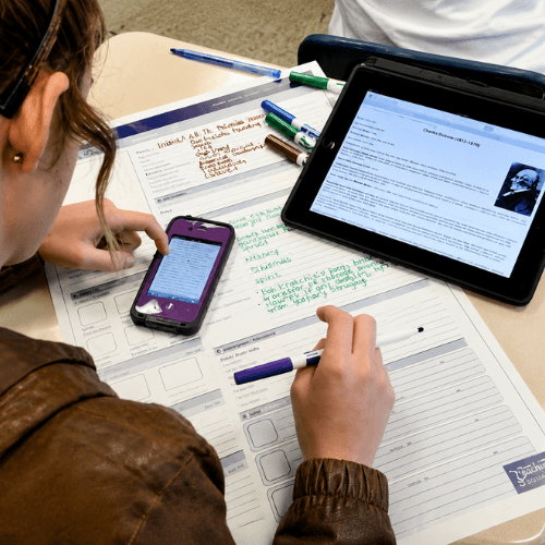 Student using a laptop, smartphone, and study materials at a desk, illustrating the importance of an ergonomic computer workspace.