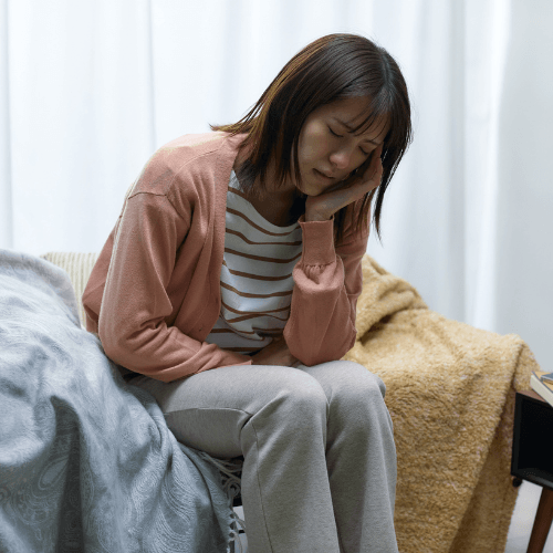 Woman sitting on a bed holding the side of her head while experiencing a myofascial headache.