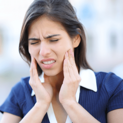 Woman holding both sides of her jaw while experiencing facial and TMJ pain.