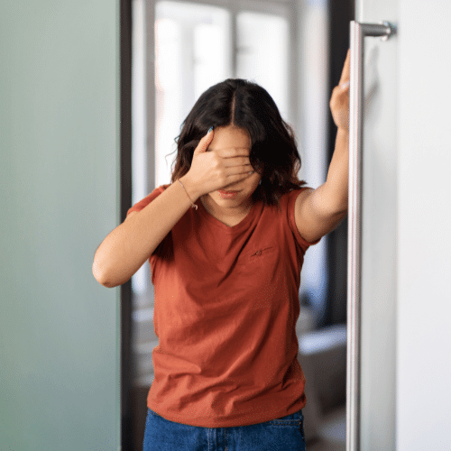 Woman holding her forehead and supporting herself against a wall while experiencing dizziness and vertigo.