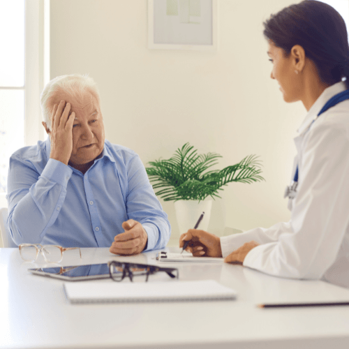 Doctor consulting with an older patient experiencing headache pain during a medical evaluation.